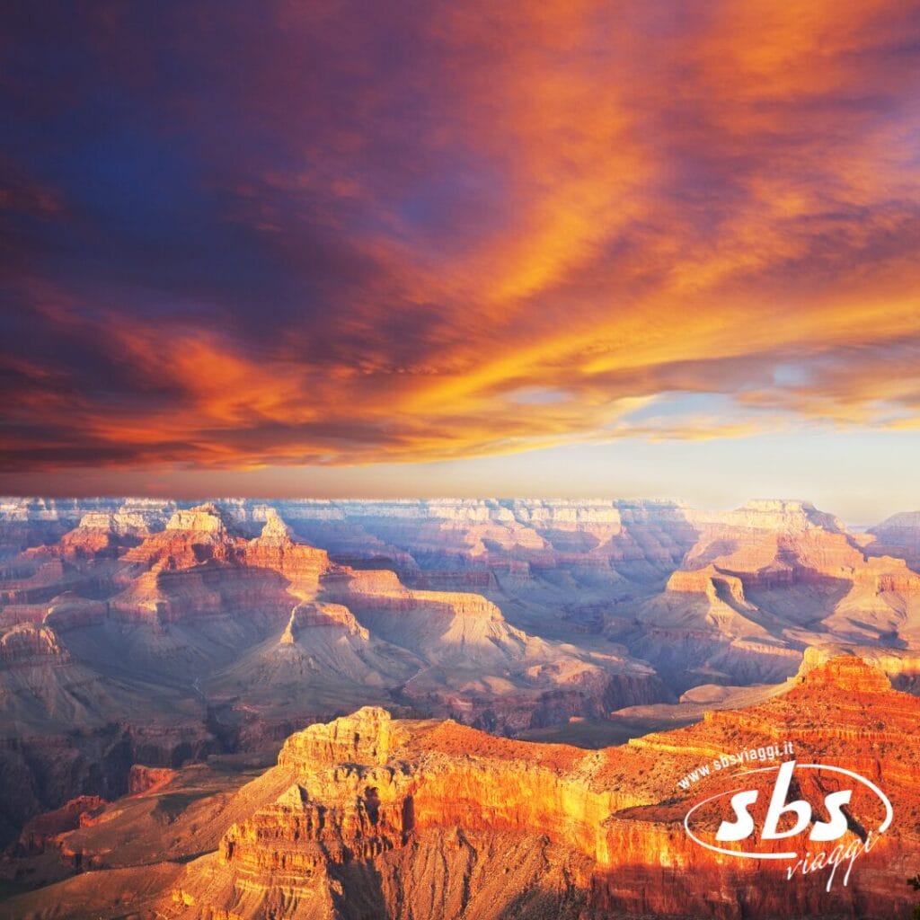 Un'ampia vista del Grand Canyon al tramonto, con le sue suggestive nuvole arancioni nel cielo e la luce del sole che illumina le formazioni rocciose del canyon: uno spettacolo naturale che sembra imperdibile anche per chi vive nella vivace Los Angeles.