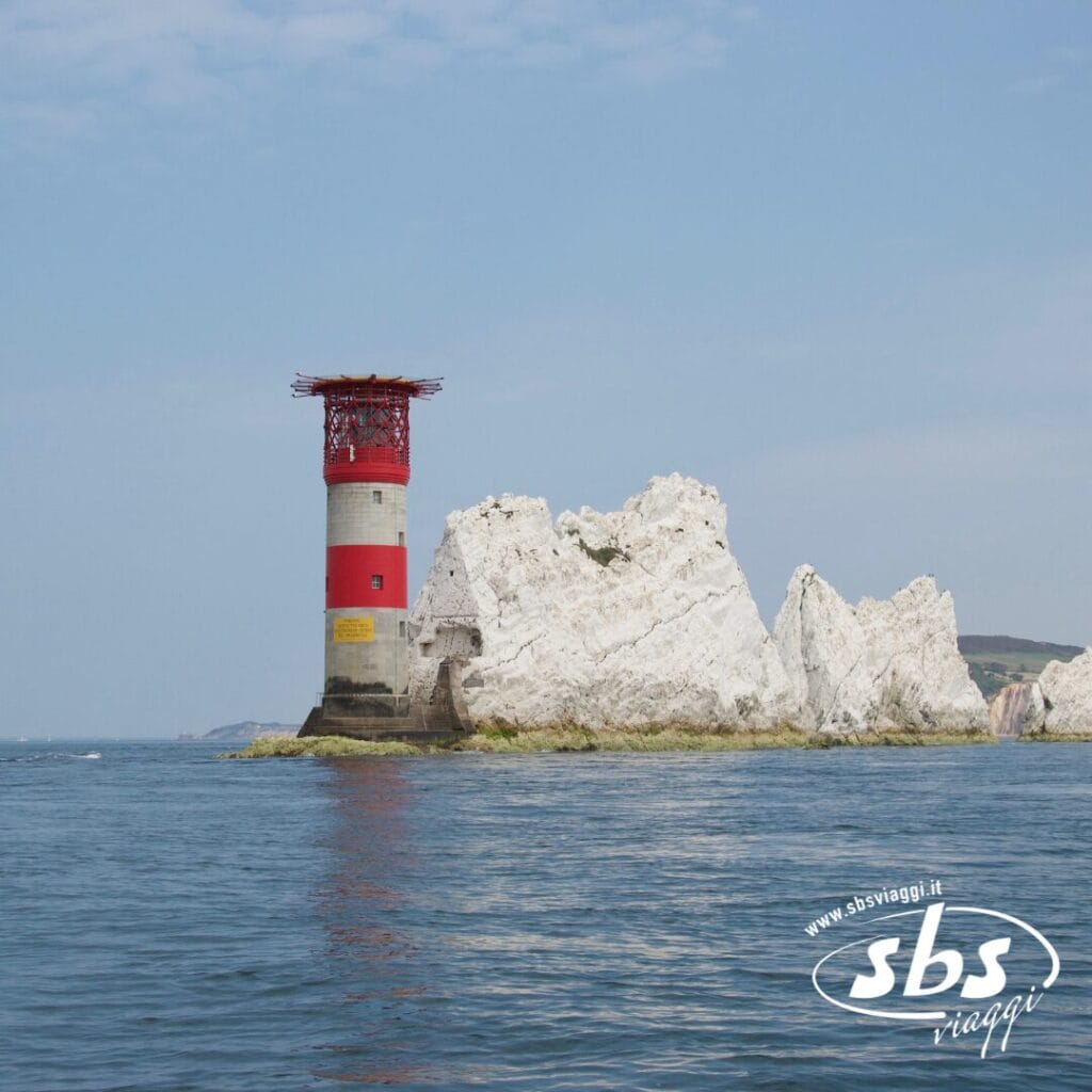 Un faro a strisce rosse e bianche si erge su una formazione rocciosa circondata da un mare calmo sotto un cielo limpido, offrendo una vista pittoresca tipica delle Isole Scozia e una tappa popolare durante un Tour Scozia.