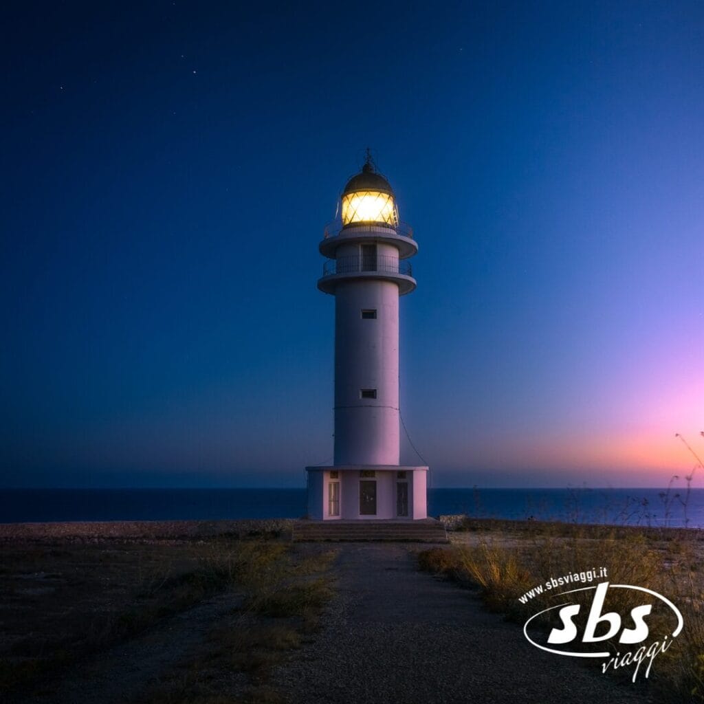 Un alto faro bianco con la luce accesa si erge in riva al mare al tramonto, sotto un cielo limpido nell'incantevole isola di Orcadi, con il logo di SBS Viaggi in un angolo: l'ispirazione perfetta per il tuo prossimo Tour Scozia.