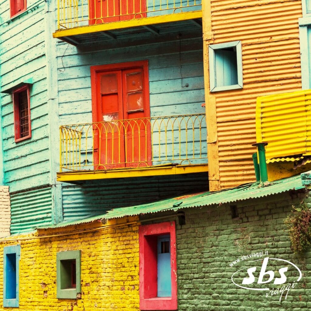 Facciata colorata di un edificio a Buenos Aires con pareti, porte e finestre dipinte di rosso, giallo, blu e verde, e un piccolo balcone con ringhiera gialla.