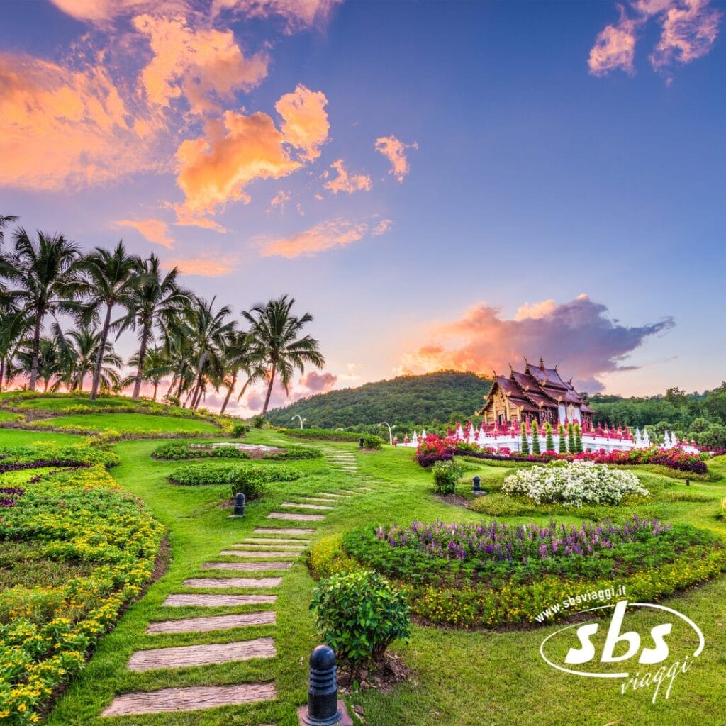 Un giardino paesaggistico con sentieri in pietra, palme, aiuole colorate e un padiglione tradizionale sotto un vivace cielo al tramonto: uno scenario ideale per un'avventura del Tour Thailandia del Nord.