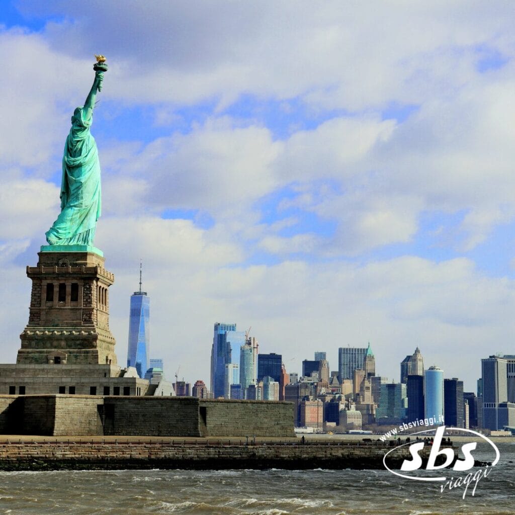 La Statua della Libertà si erge sul suo piedistallo con lo skyline di New York sullo sfondo sotto un cielo parzialmente nuvoloso: una tappa obbligata per qualsiasi avventura turistica a New York.