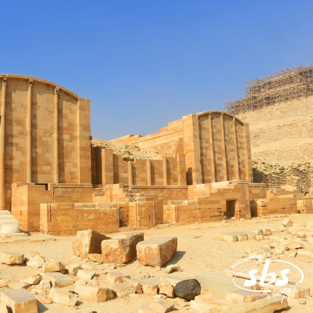 Antica struttura in pietra con grandi colonne verticali e rocce sparse in primo piano, sullo sfondo di un cielo azzurro e terso in un paesaggio desertico, che evoca la bellezza senza tempo dell'Antico Egitto e ricorda le viste di una Crociera sul Nilo.