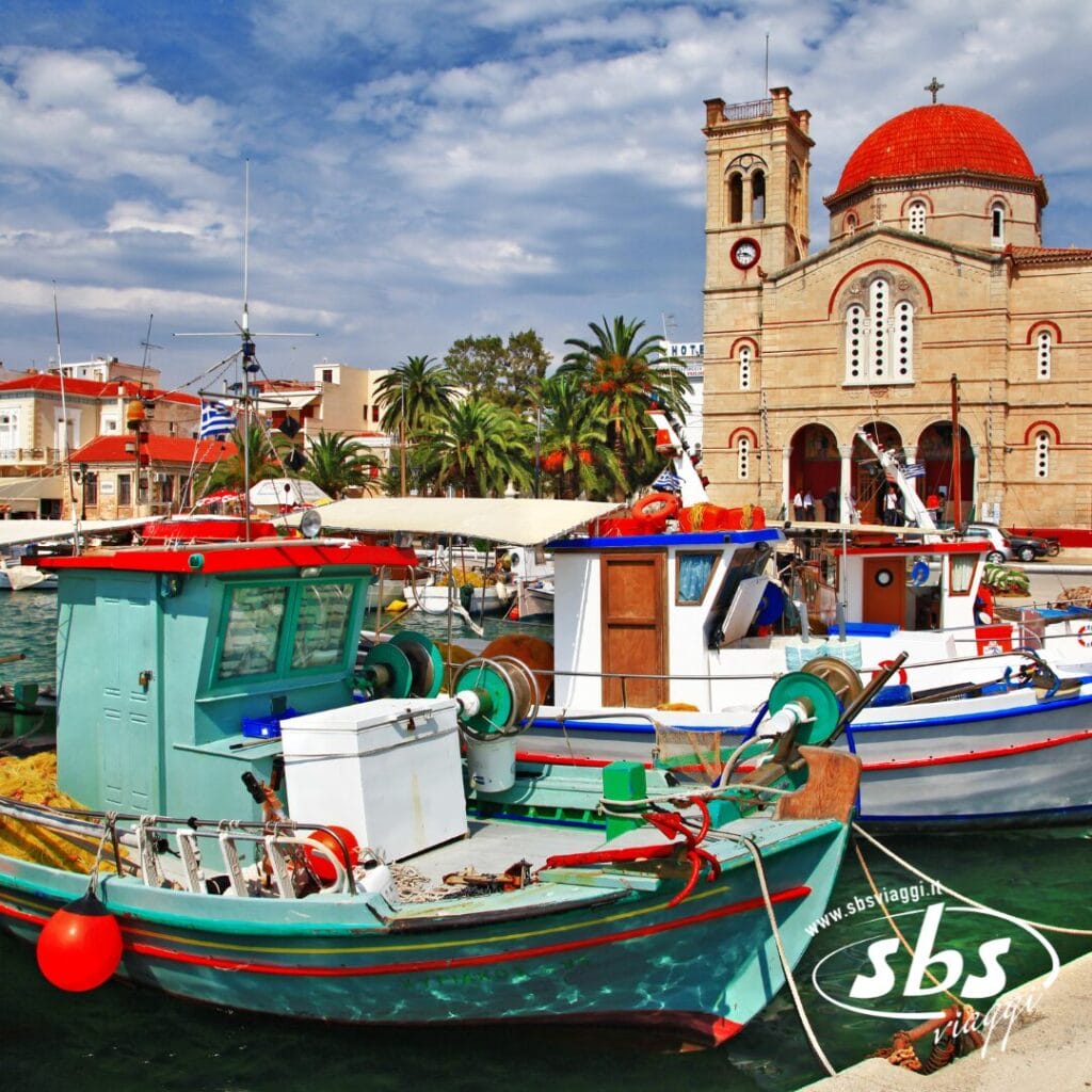 Colorate barche da pesca attraccate in un porto delle Isole Saroniche, con una grande chiesa con cupola rossa e orologio sullo sfondo sotto un cielo parzialmente nuvoloso: perfetto per il tuo prossimo Tour Grecia o per l'esplorazione della Grecia Classica.