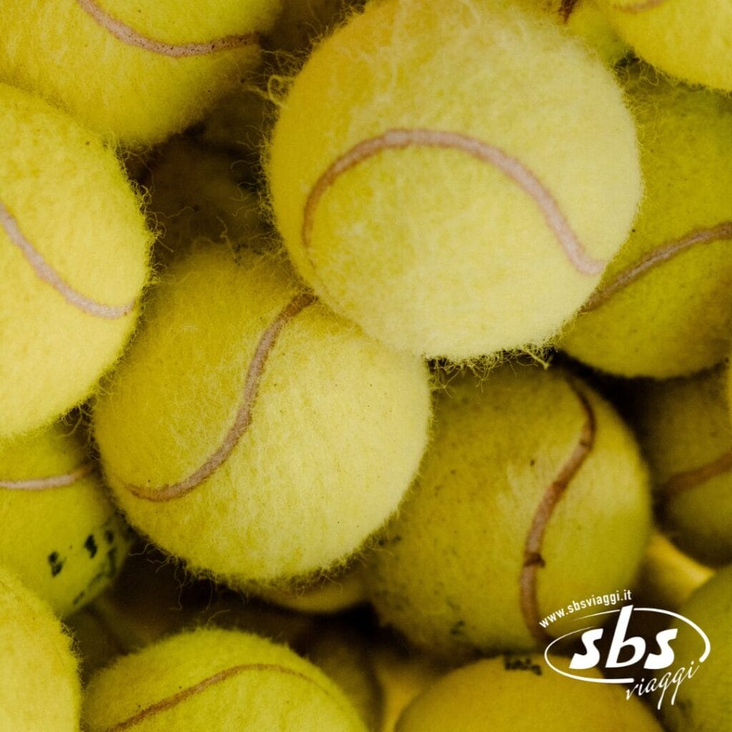 Un primo piano di una pila di palline da tennis gialle, con il logo SBS Viaggi nell'angolo in basso a destra, cattura l'emozione del Tennis Grand Tour 2025.