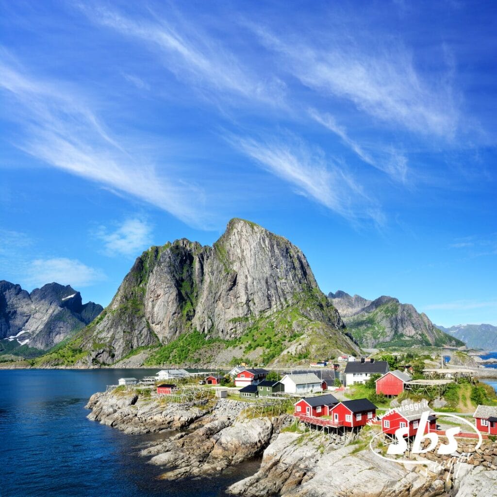 Pittoresco villaggio costiero con casette rosse sulla costa rocciosa, montagne verdi sullo sfondo e cielo azzurro con nuvole vaporose: perfetto per un'avventura con il Tour Scozia Orcadi.
