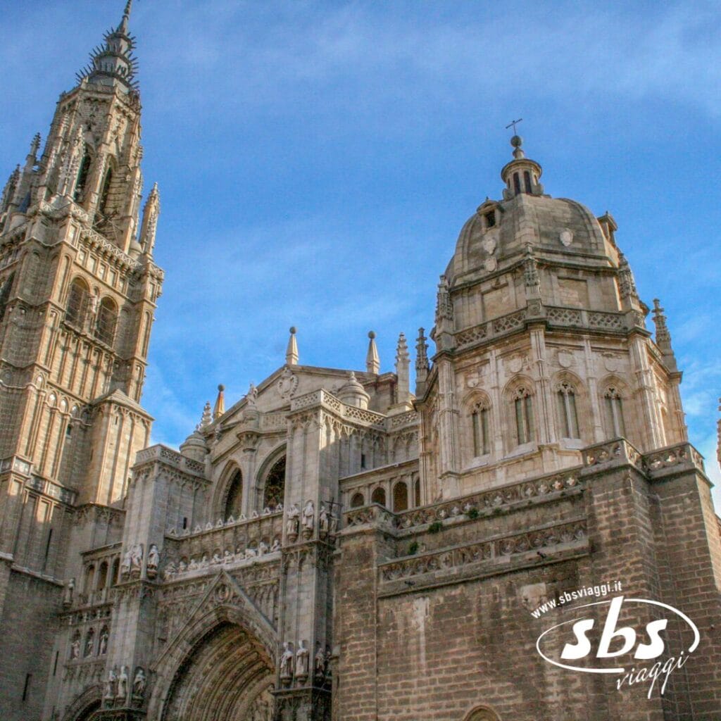 Vivi il tour di una cattedrale gotica con guglie e archi decorati che si stagliano contro un cielo azzurro, catturando le meraviglie della Spagna Medievale. Il logo di SBS Viaggi campeggia elegantemente nell'angolo in basso a destra, aggiungendo un tocco di distinzione.