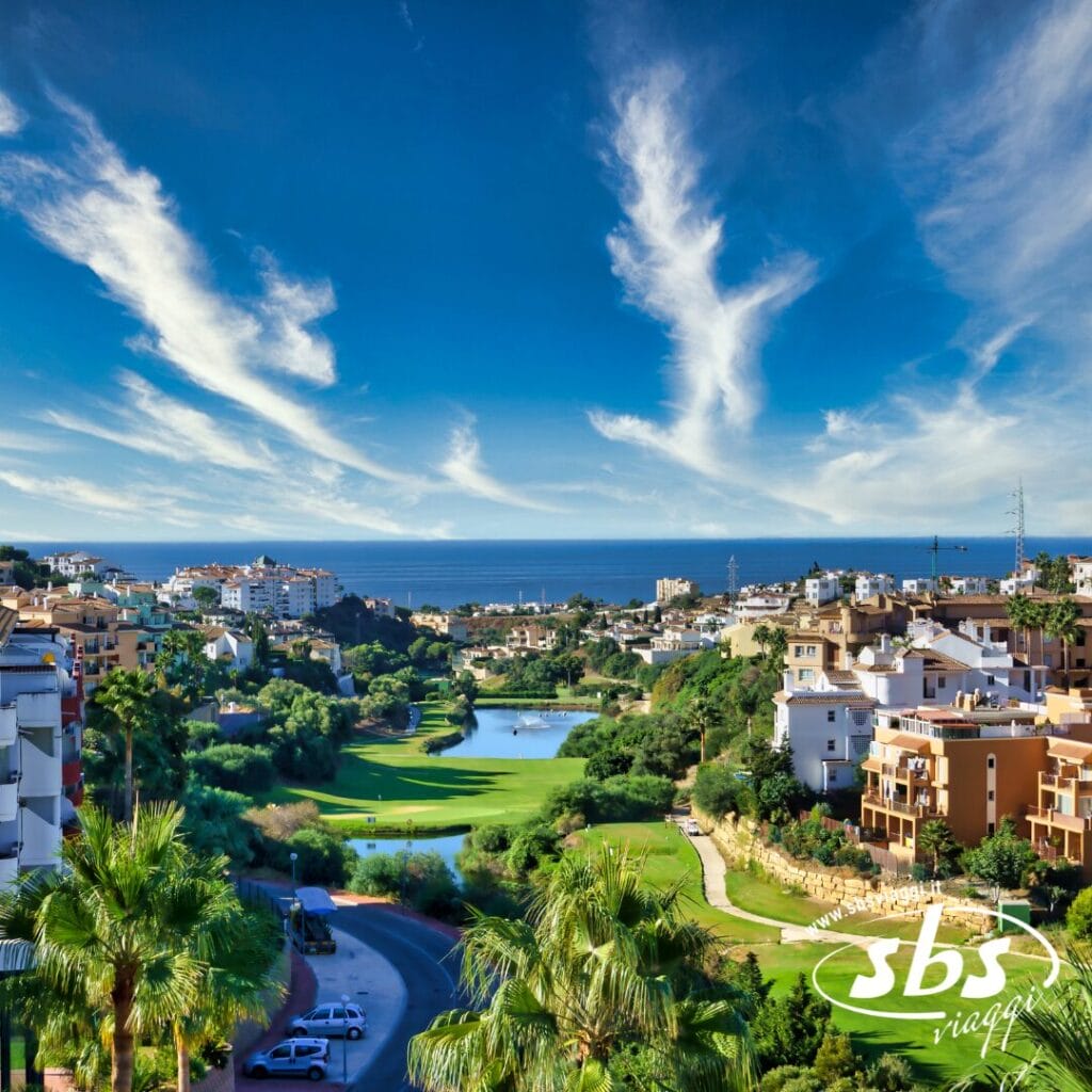 Godetevi la vista panoramica di una città costiera dell'Andalusia, dove edifici e vegetazione lussureggiante circondano un campo da golf incontaminato sotto un cielo azzurro brillante con nuvole leggere. Una tappa perfetta del vostro tour dell'Andalusia per esplorare le sue splendide attrazioni.