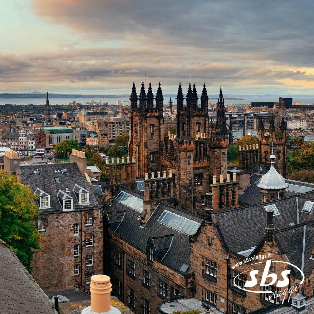 Vista della città di Edimburgo con edifici storici dall'architettura gotica sotto un cielo nuvoloso, con il mare visibile in lontananza: una tappa straordinaria di qualsiasi avventura con Orcadi o Tour Scozia.