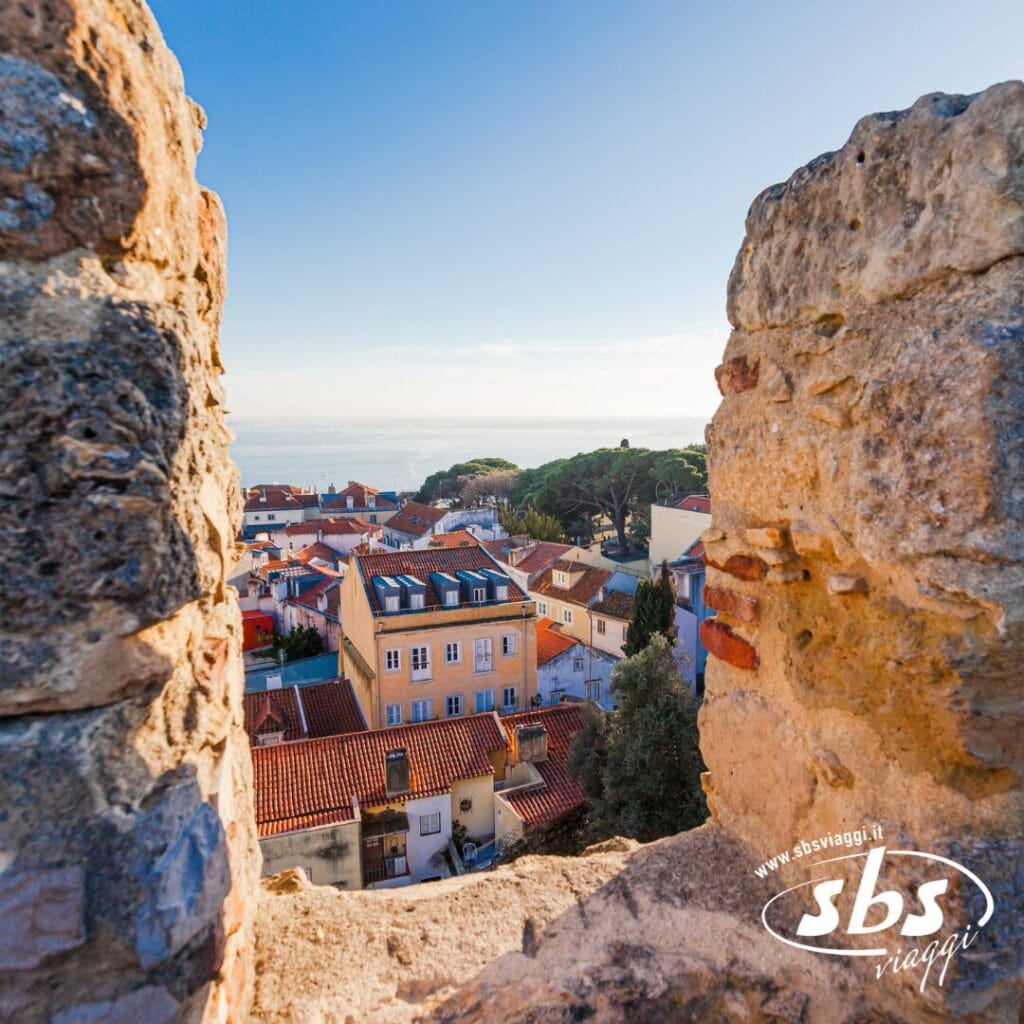 Scopri i tetti vivaci e il fascino costiero durante la tua vacanza in Portogallo, dove edifici colorati e il mare ti chiamano, incorniciati perfettamente attraverso un'apertura in un muro di pietra.