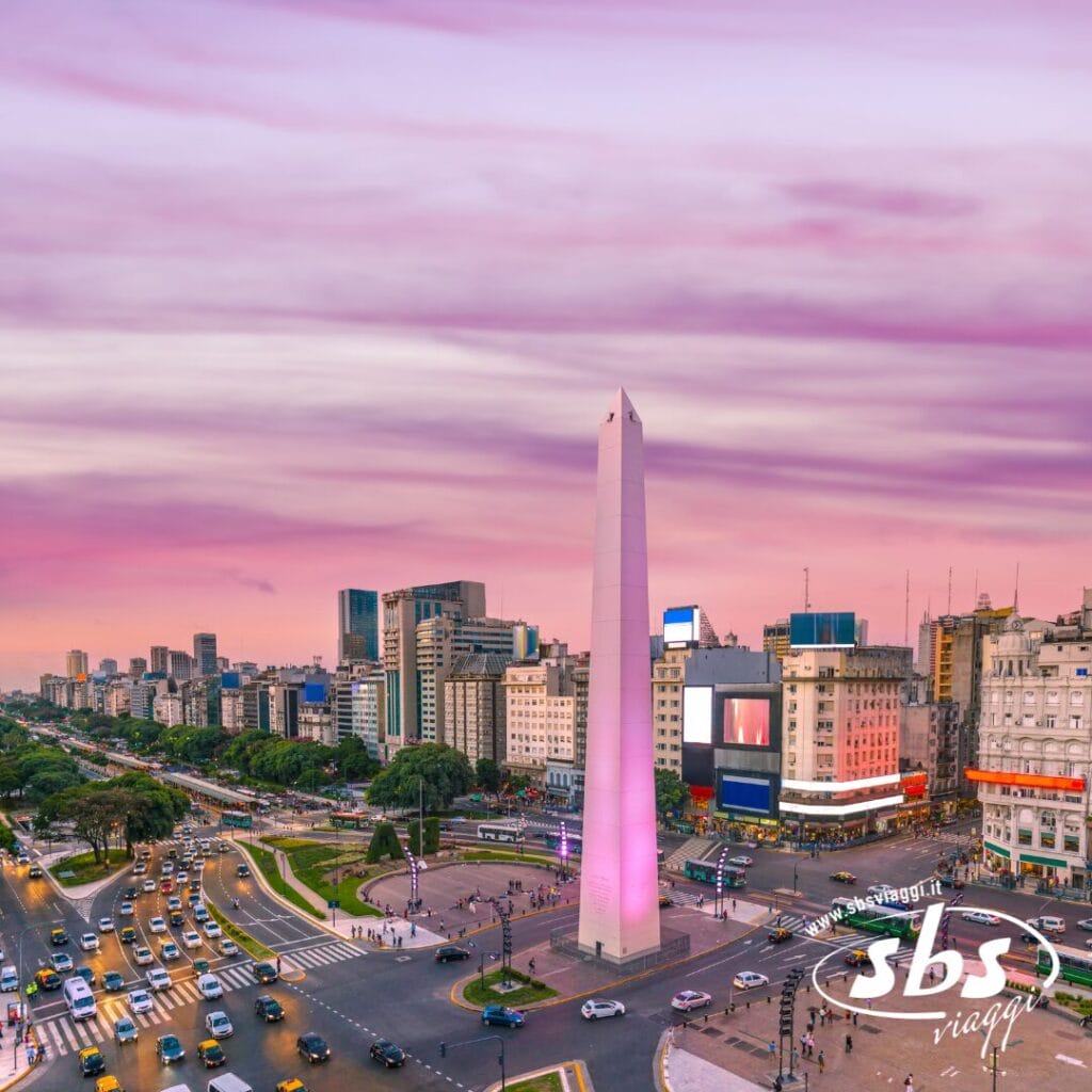 Vista aerea dell'Obelisco di Buenos Aires in una piazza trafficata della città al tramonto, con il traffico e gli edifici circostanti sotto un cielo rosa e viola, che cattura lo spirito vibrante dell'Argentina.