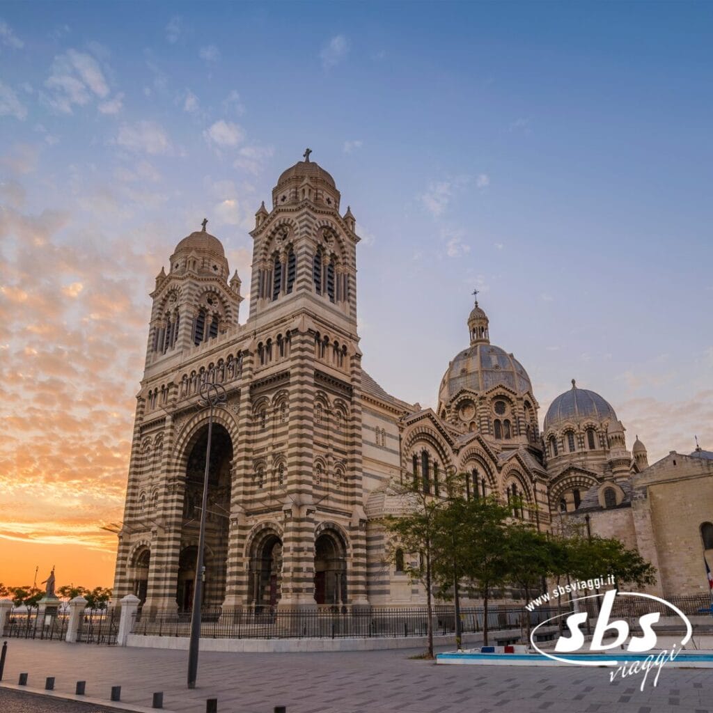 L'immagine mostra la Cattedrale di Marsiglia, un edificio monumentale con intricate decorazioni in pietra, sotto un cielo con nuvole sparse durante il tramonto, catturando l'essenza di un'avventura di trekking urbano.