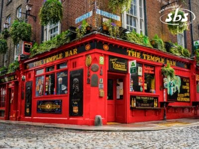 Un edificio rosso acceso all'angolo con insegne che recitano "The Temple Bar", piante sospese, poster e strade acciottolate di fronte: una vera icona tra le Bellezze d'Irlanda per qualsiasi viaggio in Irlanda.
