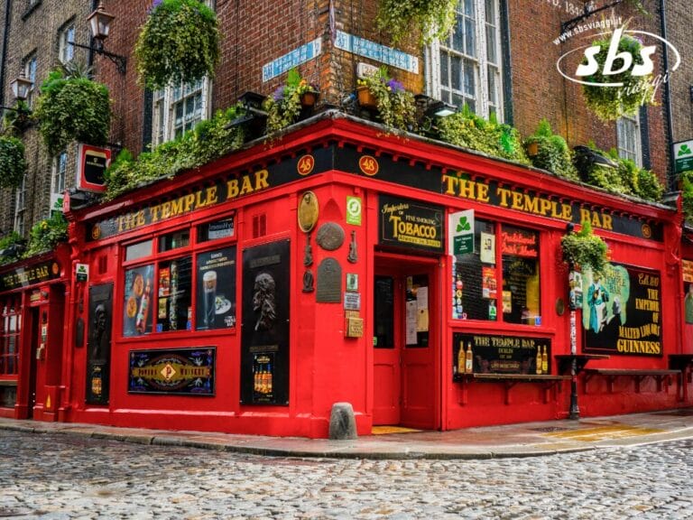 Un edificio rosso acceso all'angolo con insegne che recitano "The Temple Bar", piante sospese, poster e strade acciottolate di fronte: una vera icona tra le Bellezze d'Irlanda per qualsiasi viaggio in Irlanda.