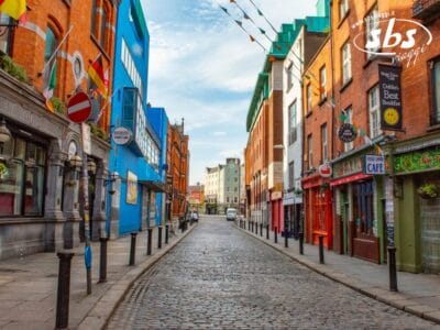 Una strada acciottolata in Irlanda fiancheggiata da edifici colorati, negozi e caffè; le bandiere sono appese in alto e la strada è vuota, evocando il fascino delle Isole Aran.