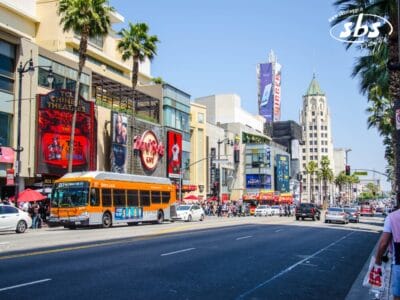 Una vista di una strada trafficata di Hollywood Boulevard a Los Angeles, con un autobus della metropolitana, pedoni, palme e tendoni dei teatri sotto un cielo limpido e luminoso: una scena che rispecchia davvero l'Essential 1924.