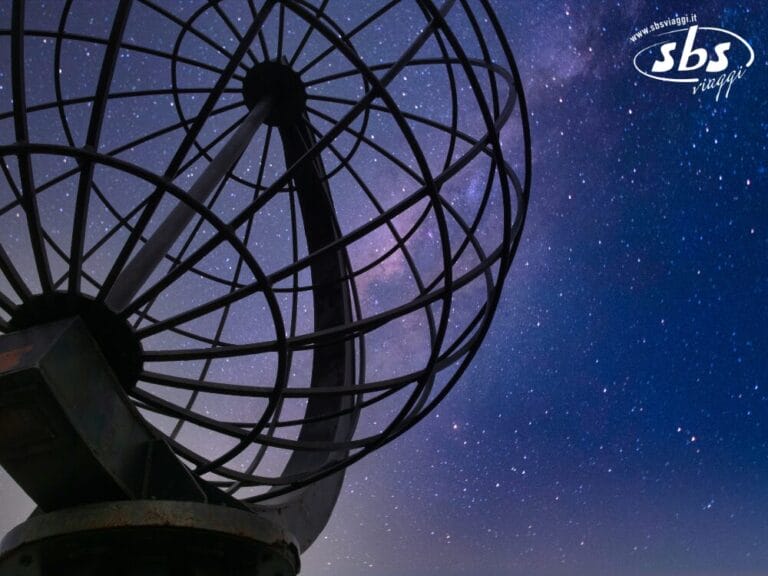 In primo piano è raffigurata una scultura a forma di globo metallico, con un cielo notturno stellato e parte della Via Lattea visibile sullo sfondo, a catturare la magia di un tour a Capo Nord. Il logo di SBS Viaggi appare nell'angolo in alto a destra.