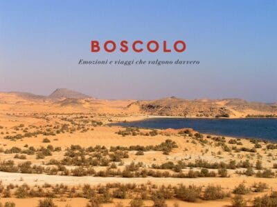 Paesaggio desertico con cespugli sparsi, un lago azzurro che ricorda il Lago Nasser, e testo: "BOSCOLO Emozioni e viaggi che valgono davvero".