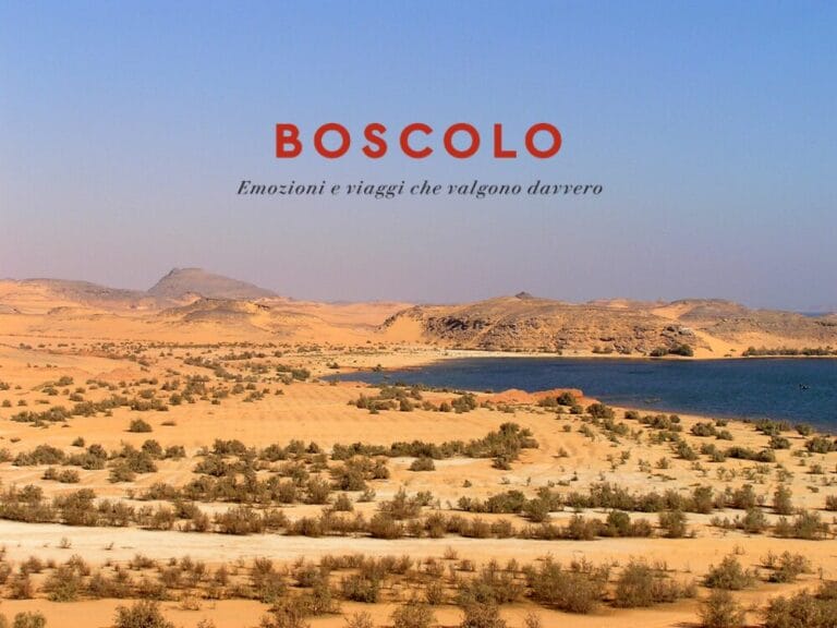 Paesaggio desertico con cespugli sparsi, un lago azzurro che ricorda il Lago Nasser, e testo: "BOSCOLO Emozioni e viaggi che valgono davvero".