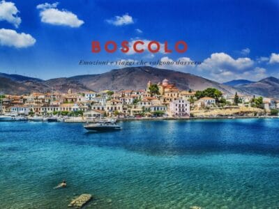 Colorata cittadina di mare con barche, montagne sullo sfondo e un nuotatore nel mare blu; il testo recita "BOSCOLO".