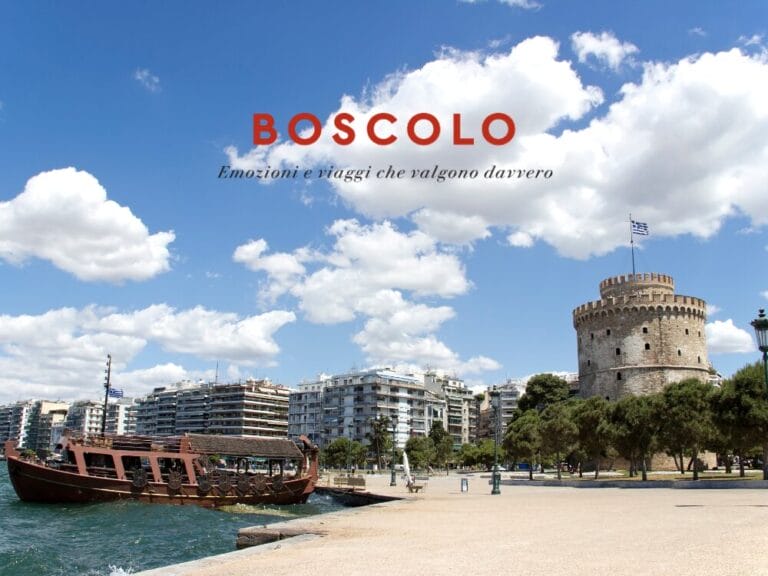 Barca di legno sul lungomare di Salonicco, con edifici moderni e la Torre Bianca sotto un cielo azzurro: perfetta per un tour nelle Terre di Alessandro Magno.