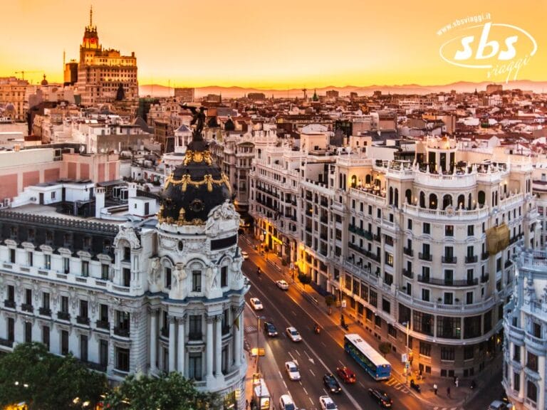 Paesaggio urbano di Madrid al tramonto, che mette in mostra le meraviglie della Gran Vía con edifici storici e traffico frenetico sotto un cielo arancione brillante, catturando l'essenza della Spagna.