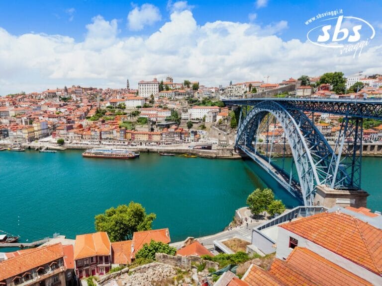 Esplora le meraviglie di Porto, in Portogallo, con una vista mozzafiato sul Ponte Dom Luís I che attraversa il fiume Duero, incorniciato da edifici dai tetti rossi sotto un cielo nuvoloso. Perfetto per il tuo prossimo viaggio!.