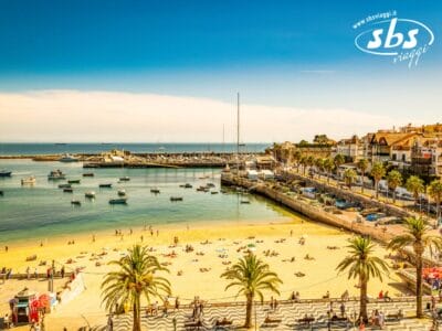 Spiaggia soleggiata con palme, barche in acqua e un porto tranquillo. Edifici e lungomare impreziosiscono questo tranquillo scenario costiero, sotto un cielo azzurro e limpido: un luogo perfetto per un tour lungo le splendide coste portoghesi.