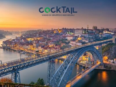 Vista di Porto al tramonto con il ponte Dom Luís I sul fiume Douro; in alto il logo del viaggio Cocktail. L'ispirazione perfetta per il vostro prossimo Viaggio Portogallo o per le vostre indimenticabili Vacanze Portogallo.