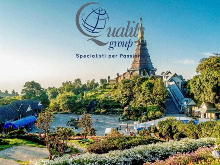 Un rigoglioso giardino con una pagoda e degli edifici in una giornata di sole evoca il fascino sereno della Thailandia del Nord, con il logo e lo slogan del "Quality group" sovrapposti.