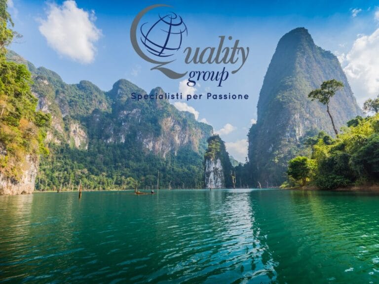 Lago turchese con alte montagne verdi sotto un cielo azzurro; logo e slogan del Quality Group sovrapposti, che evocano lo spirito delle avventure Grantour in Thailandia.