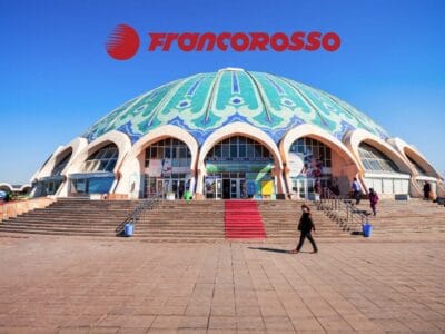 Grande edificio a cupola con ingressi ad arco, tetto decorato e persone che camminano su ampi gradini; logo Francorosso in alto: un gioiello architettonico che ricorda la Terra di Tamerlano.