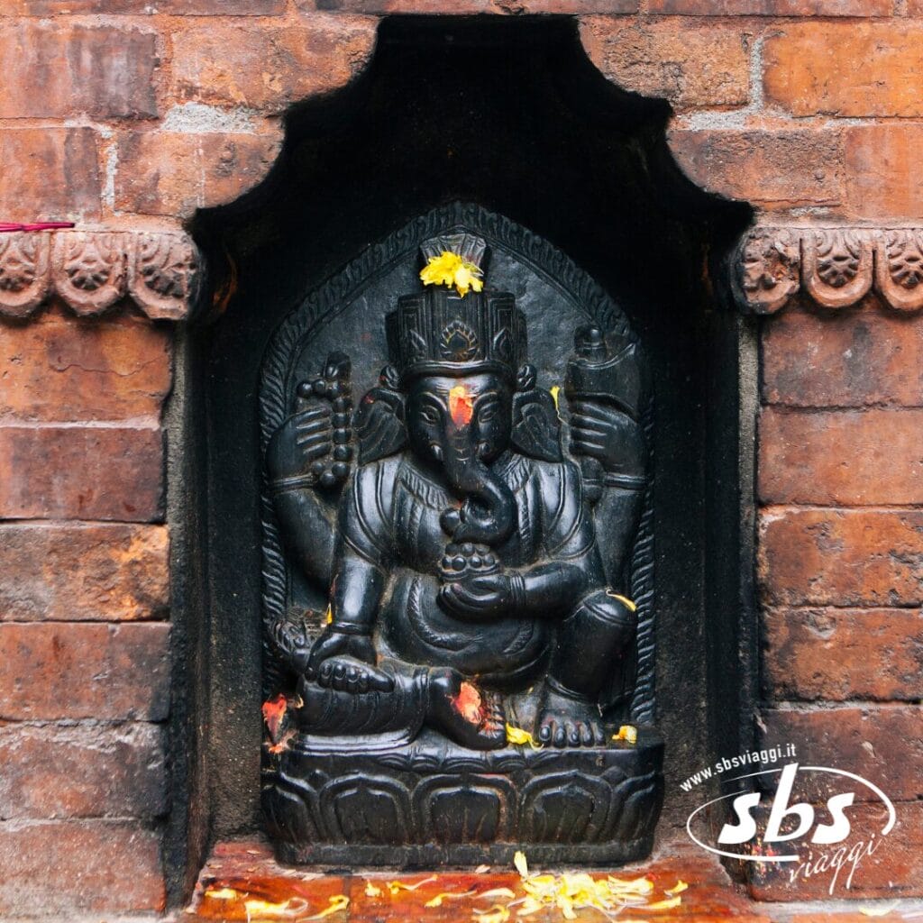 Una statua in pietra della divinità indù Ganesha è posta in una nicchia di mattoni nella Valle degli Dei in Nepal, adornata con fiori gialli e polvere rossa sulla fronte, catturando lo spirito del Festival di Dashain.