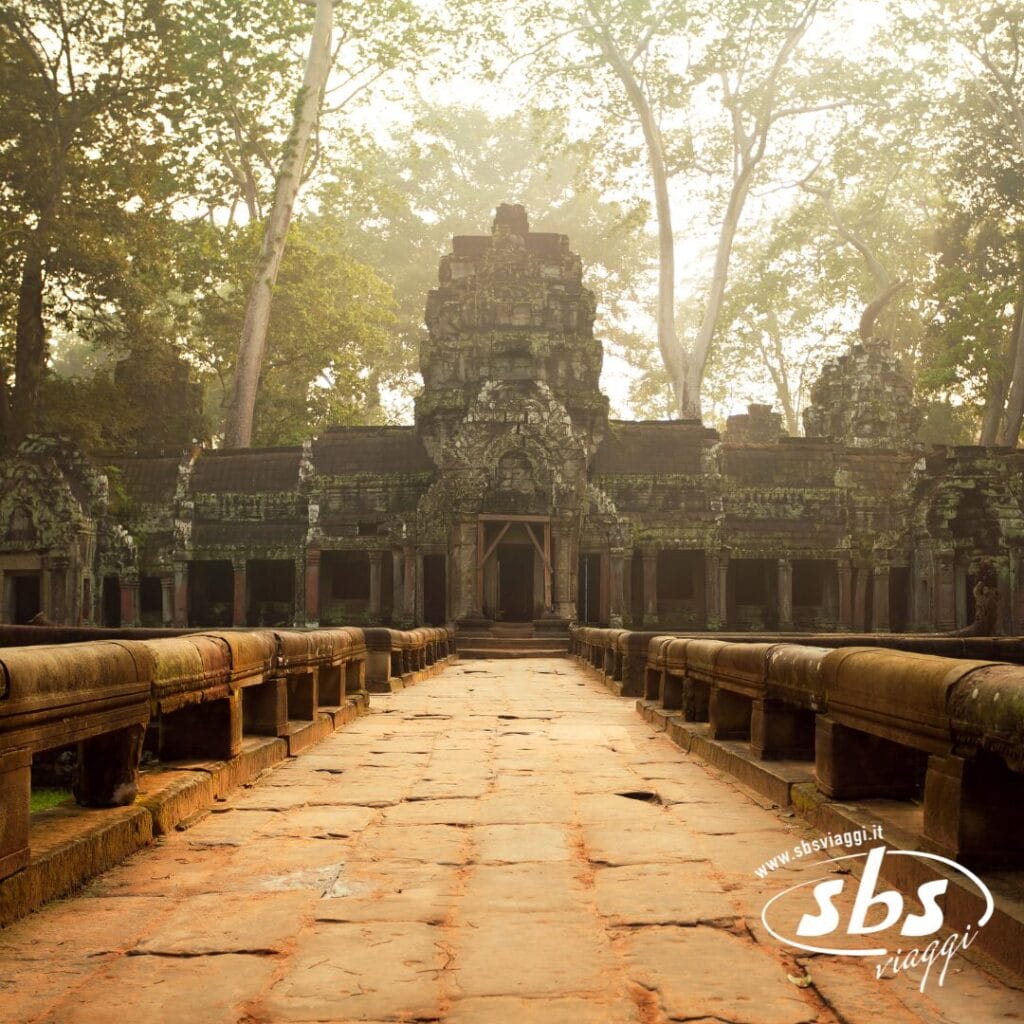 Antico tempio in pietra con incisioni dettagliate, circondato da alberi e nebbia, visto da un sentiero che conduce all'ingresso. Il logo