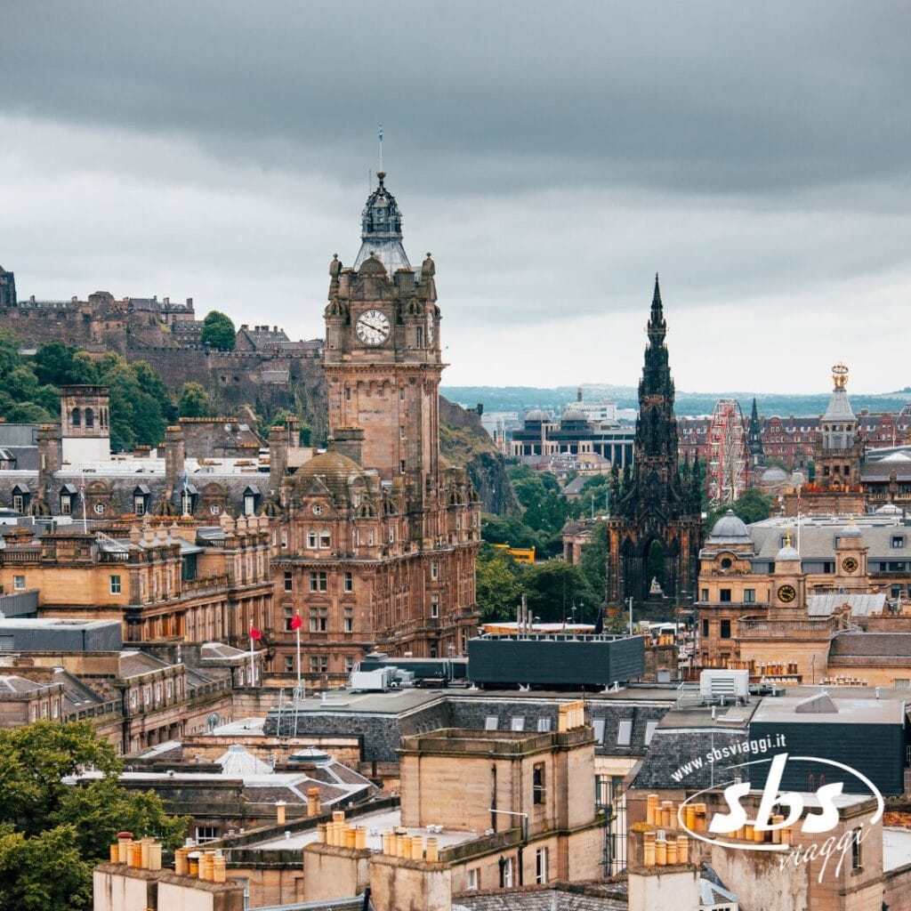 Una vista del centro di Edimburgo con la Balmoral Clock Tower, il monumento Scott, edifici storici e vegetazione in lontananza sotto un cielo nuvoloso: un'introduzione perfetta prima di esplorare le Highlands o di partecipare a un indimenticabile Tour Scozia.