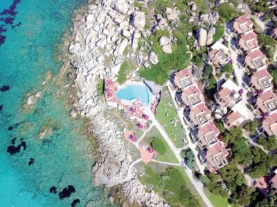 Vista aerea di una località balneare con Bozza automatica, costa rocciosa, acqua turchese e cristallina e villette a schiera con tetti rossi.