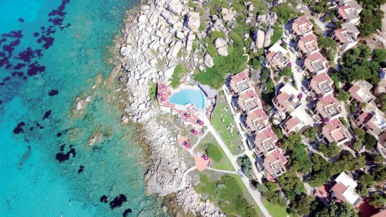 Vista aerea di una località balneare con Bozza automatica, costa rocciosa, acqua turchese e cristallina e villette a schiera con tetti rossi.