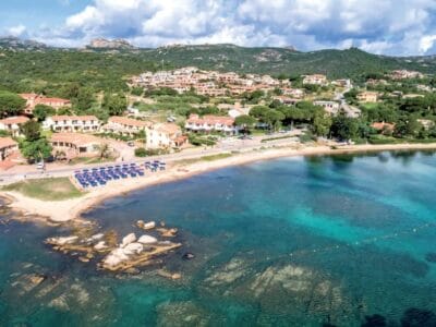 Vista aerea di un villaggio costiero con spiaggia sabbiosa, acqua turchese e verdi colline sullo sfondo, immortalata in una bozza automatica per preservarne la bellezza naturale.