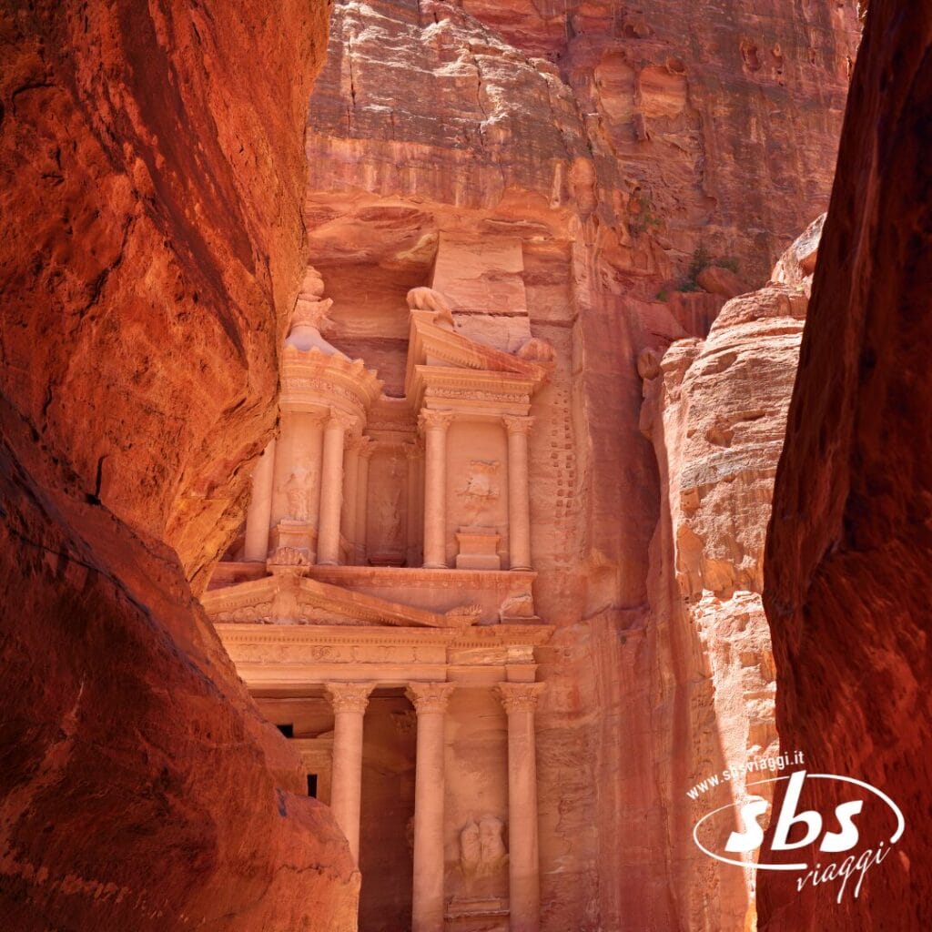 Vista dell'antico Tesoro di Petra scavato nelle scogliere di roccia rossa, parzialmente incorniciato da uno stretto canyon: una delle meraviglie della Giordania da non perdere durante un tour della Giordania.