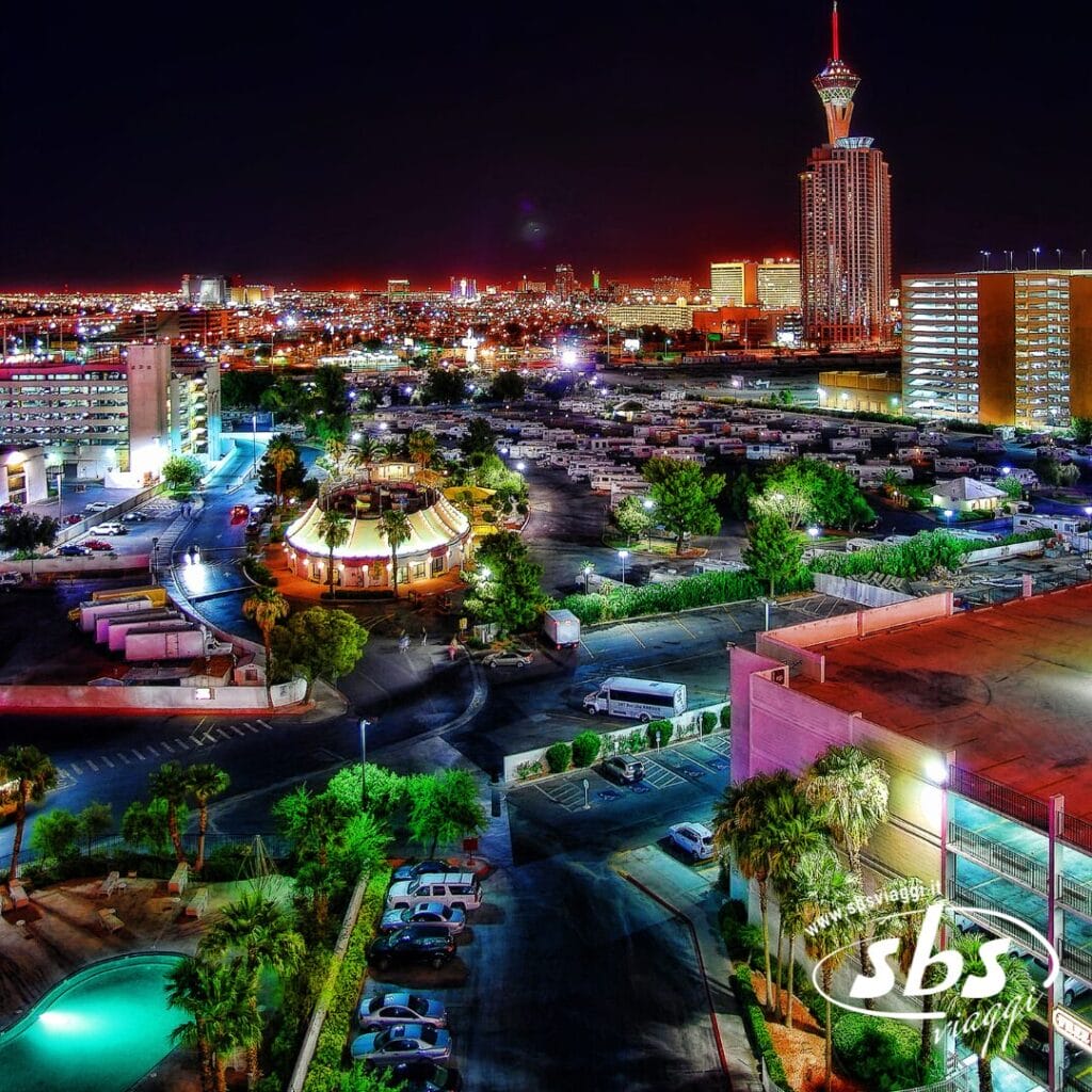 Vista aerea di un paesaggio urbano illuminato di notte, con grattacieli, un parco camper e luci al neon, con la Stratosphere Tower sullo sfondo: uno scenario mozzafiato lungo il Tour del Golden West.