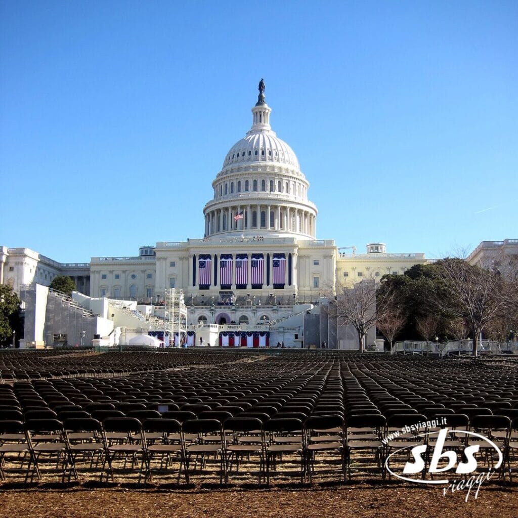 File di sedie vuote sono disposte davanti al Campidoglio degli Stati Uniti, decorate con bandiere americane, sotto un cielo azzurro e terso: una scena solenne che potrebbe far parte di qualsiasi grand tour, dalle cascate del Niagara allo Splendore dell'Est.