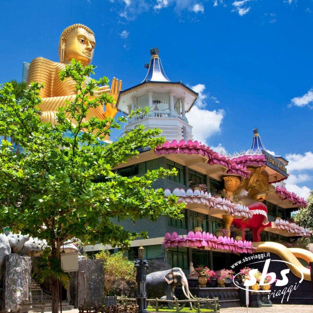 Una grande statua dorata del Buddha si trova dietro un tempio decorato con fiori di loto rosa, sotto un cielo azzurro nuvoloso: uno spettacolo maestoso durante un tour naturalistico in Sri Lanka.