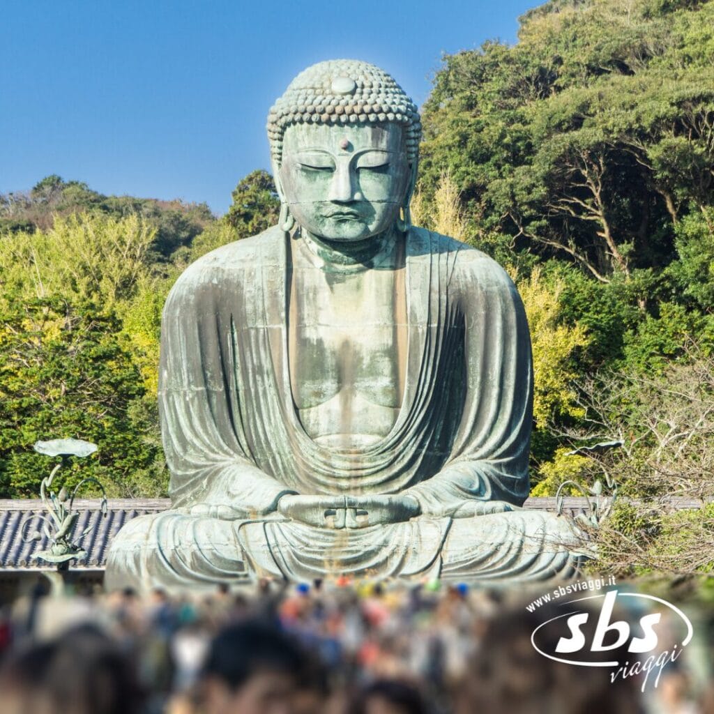 Una grande statua in bronzo del Buddha è immersa nel verde in Giappone, con una folla radunata ai suoi piedi sotto un cielo limpido, evocando lo spirito delle celebrazioni del Matsuri.