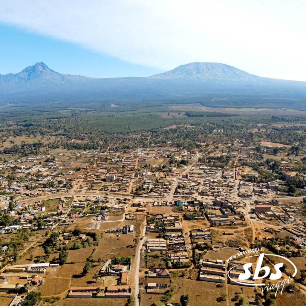 Vista aerea di una città del Kenya con edifici sparsi, campi e due grandi montagne sullo sfondo, tra cui il maestoso Kilimangiaro.