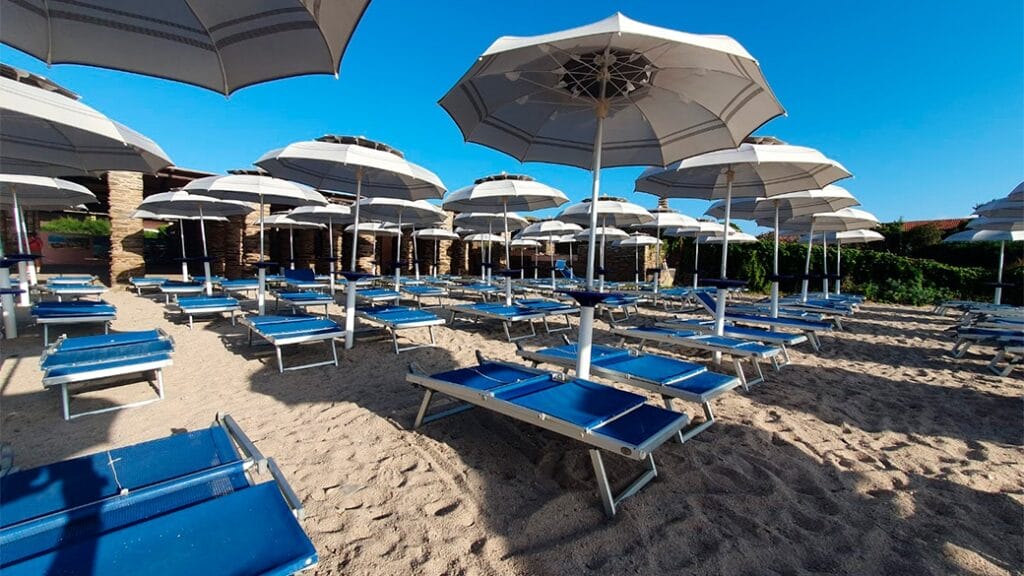 File di lettini blu e ombrelloni bianchi sulla spiaggia sabbiosa sotto un cielo azzurro e limpido, il luogo perfetto per rilassarsi e bere bozza automatica.