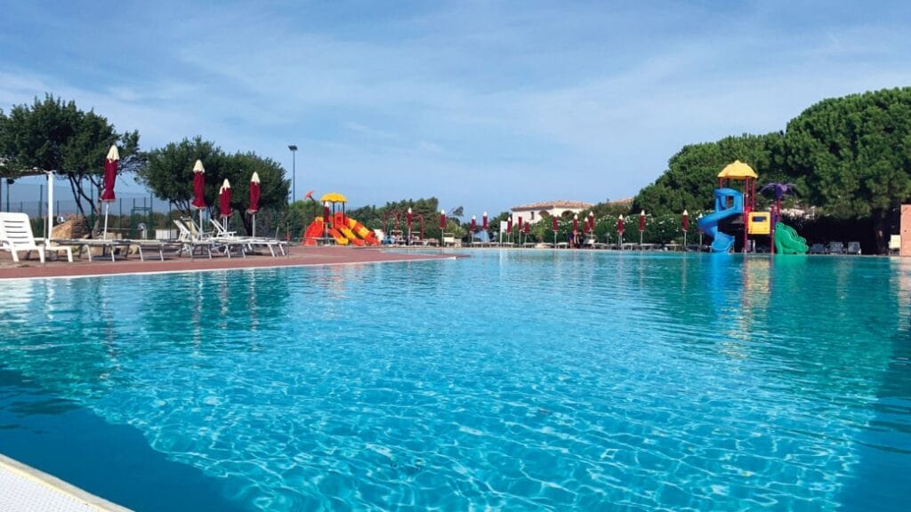Ampia piscina all'aperto con sedie a sdraio, ombrelloni e colorati scivoli d'acqua sotto un limpido cielo azzurro: perfetta per una giornata di relax o per godersi il divertimento della Bozza automatica con amici e familiari.