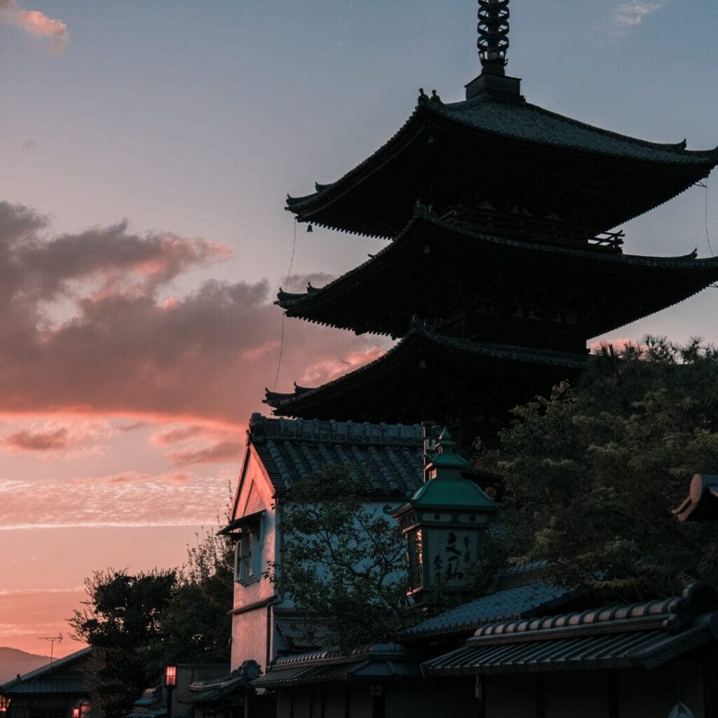 Una tradizionale pagoda giapponese che si staglia contro il cielo al tramonto, con tetti e alberi in primo piano, catturando la serena bellezza del Giappone, spesso apprezzata durante un Tour Giappone.