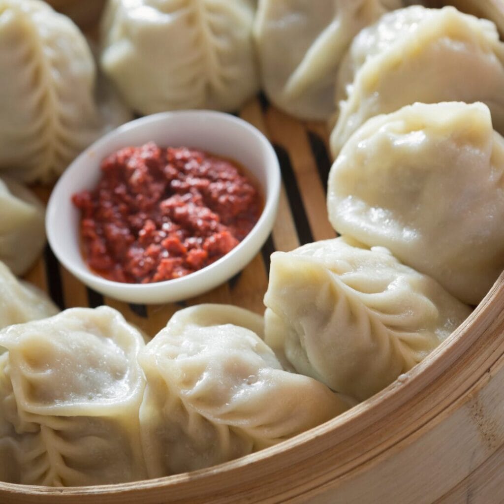 Una vaporiera di bambù piena di ravioli al vapore disposti attorno a una piccola ciotola di salsa rossa, perfetta da gustare dopo un'avventura nel Tour Kazakistan.