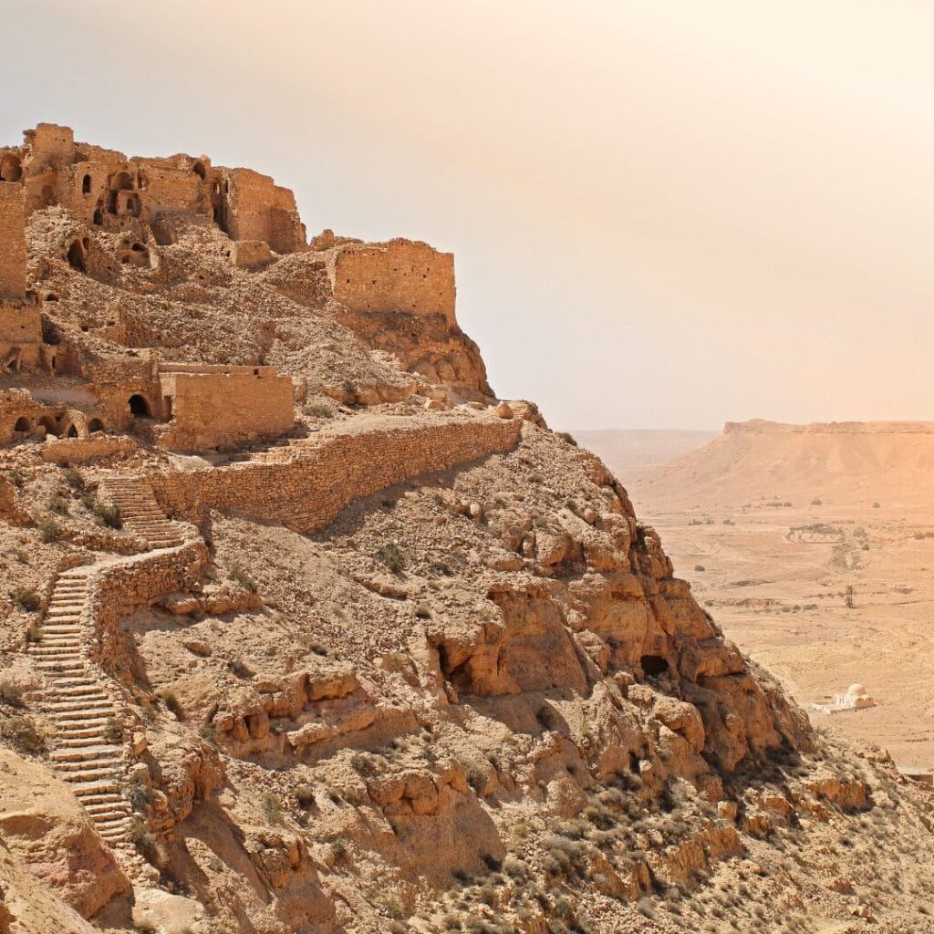 Antiche rovine in pietra su una collina rocciosa in Tunisia dominano un vasto e arido paesaggio desertico sotto un cielo nebbioso: l'ideale per avventure in fuoristrada verso oasi nascoste.