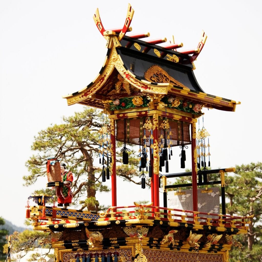 Un tradizionale carro allegorico giapponese del festival matsuri, decorato con elaborate decorazioni in oro e rosso, nappe pendenti e intagli elaborati, sullo sfondo di alberi verdi in Giappone.
